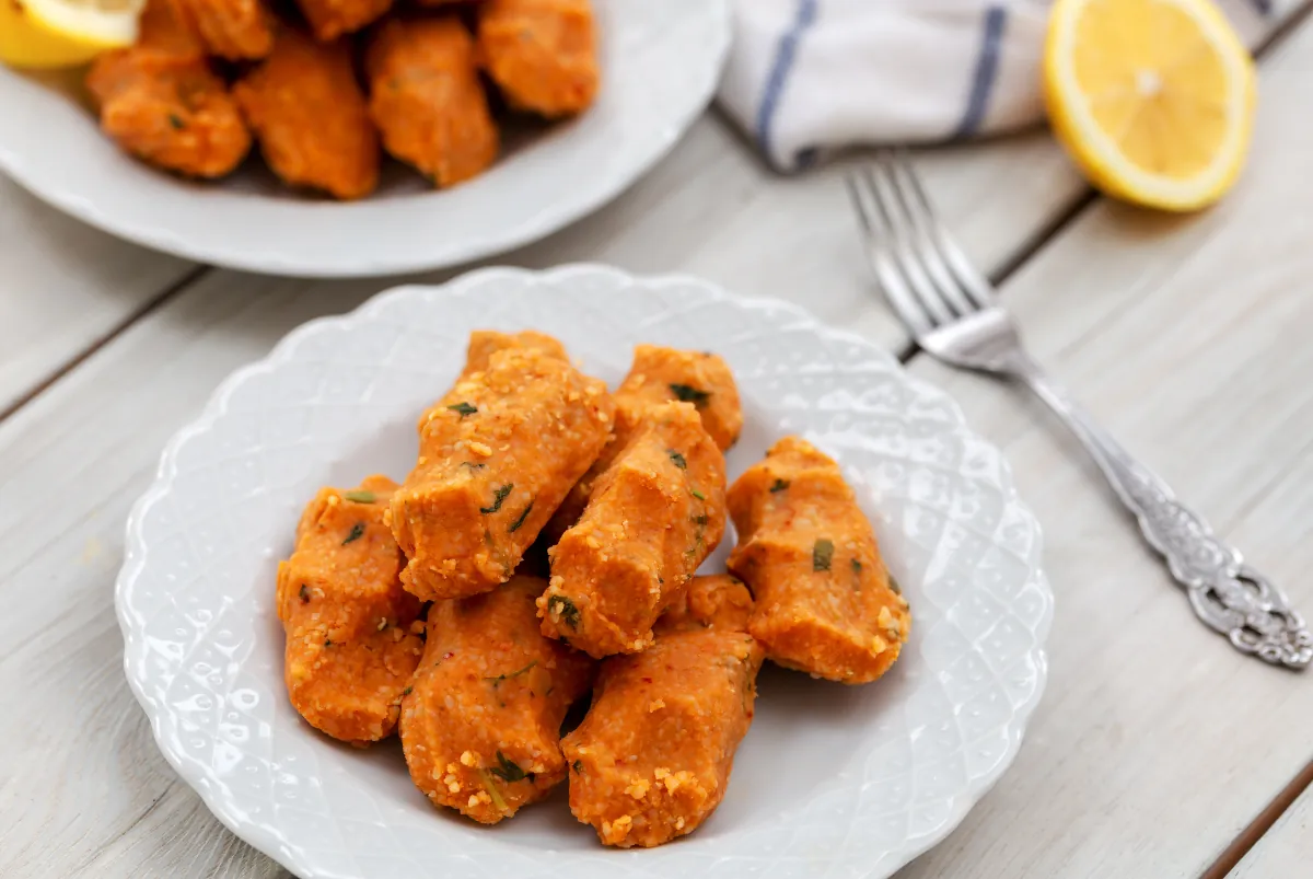 Mercimek köftesi, red lentil and bulgur patties flecked with parsley, on a white plate with a fork and lemon halves.